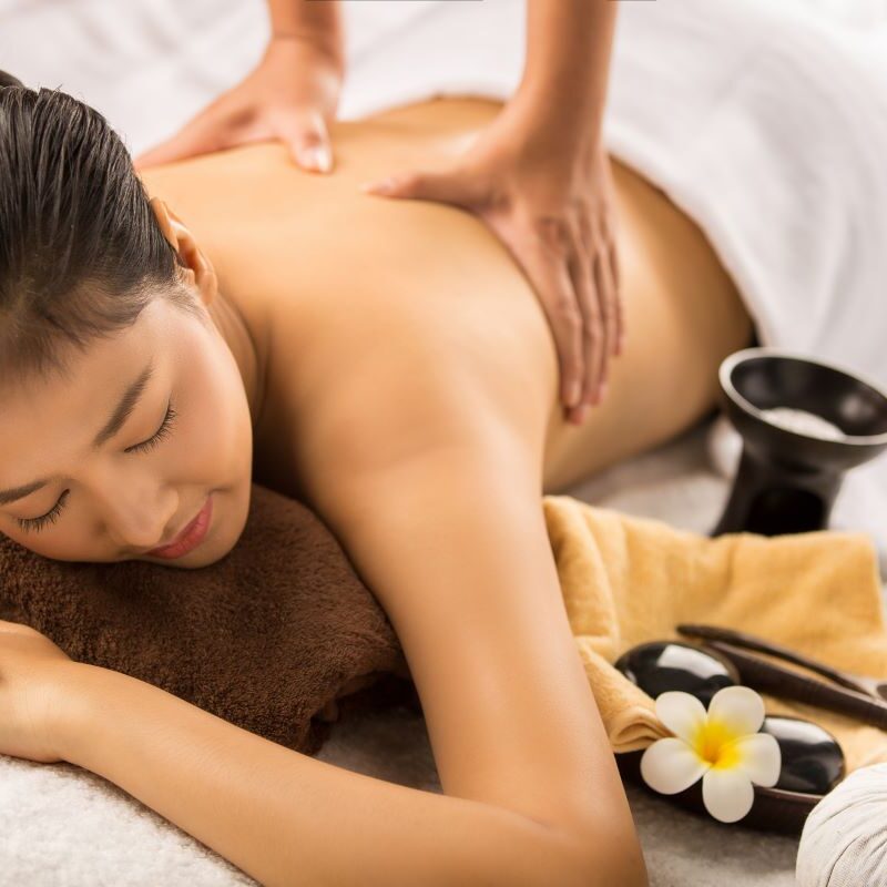 A woman receiving a relaxing back massage at a spa, surrounded by decorative flowers and towels - massage